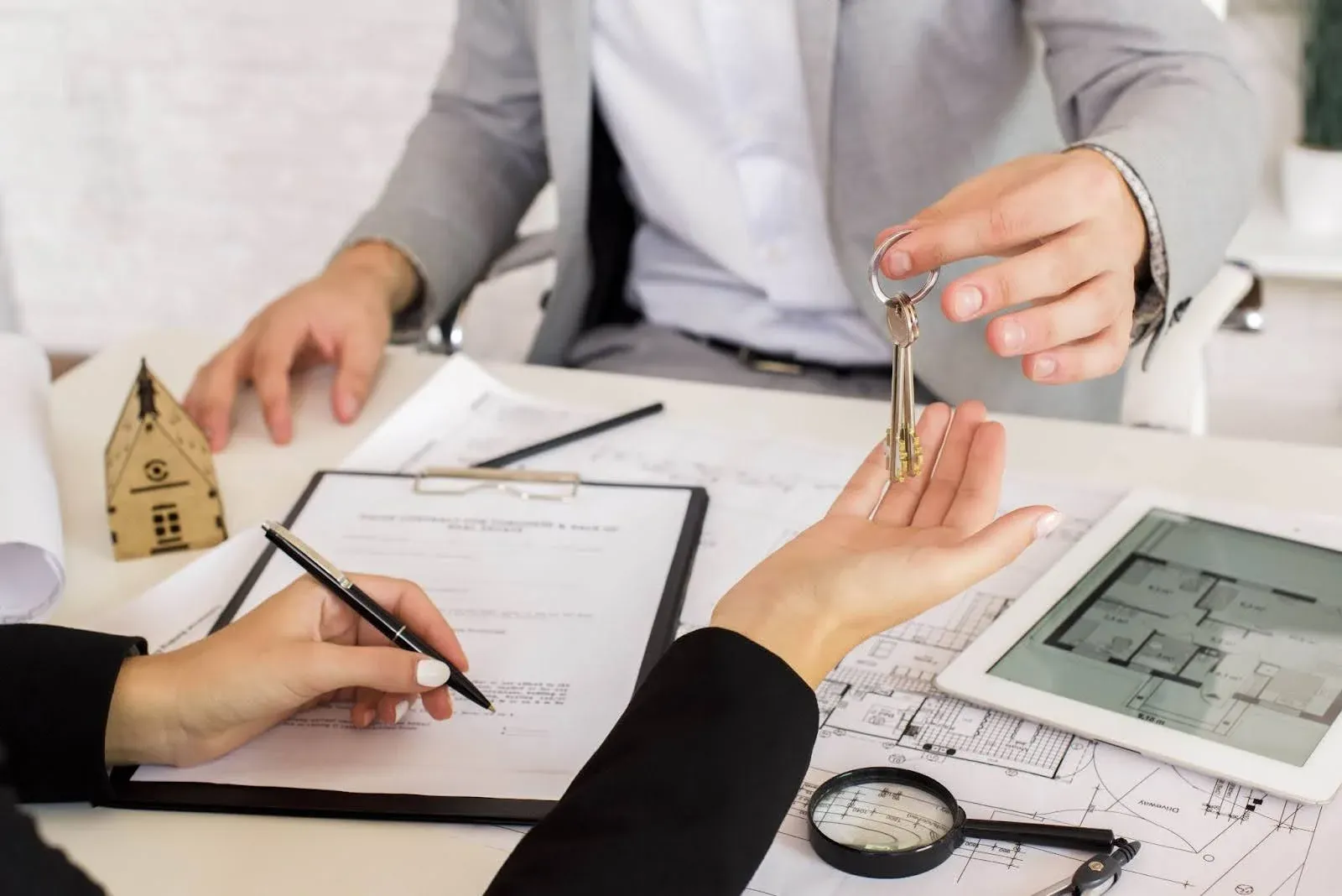 Real estate agent handing over keys to a woman signing contract.webp