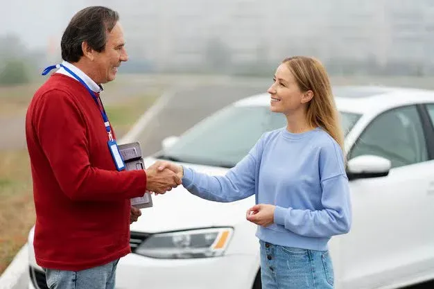 a man and woman shaking hands with a car behind them.webp