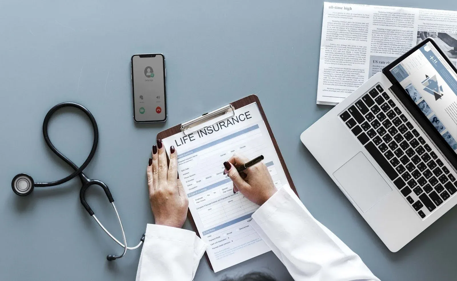 doctor filling form with a phone, stethoscope and laptop near it.webp