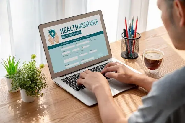 person filling a health insurance form on a laptop.webp
