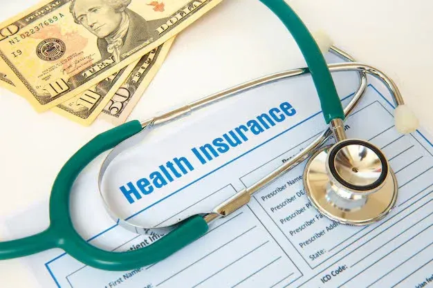 stethoscope on top of a health insurance form and some money.webp